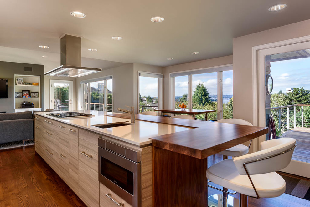 Open concept kitchen - mid-sized contemporary single-wall medium tone wood floor open concept kitchen idea in Seattle with flat-panel cabinets, light wood cabinets, solid surface countertops, an island, an undermount sink, gray backsplash, subway tile backsplash and stainless steel appliances