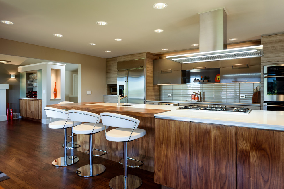 Inspiration for a large contemporary galley kitchen/diner in Seattle with an integrated sink, flat-panel cabinets, medium wood cabinets, stainless steel worktops, grey splashback, glass tiled splashback, stainless steel appliances, an island, dark hardwood flooring and brown floors.