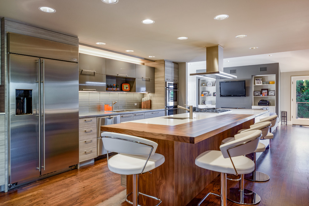 Modern inredning av ett stort kök, med en integrerad diskho, släta luckor, grått stänkskydd, stänkskydd i glaskakel, rostfria vitvaror, en köksö, grå skåp, mörkt trägolv och brunt golv