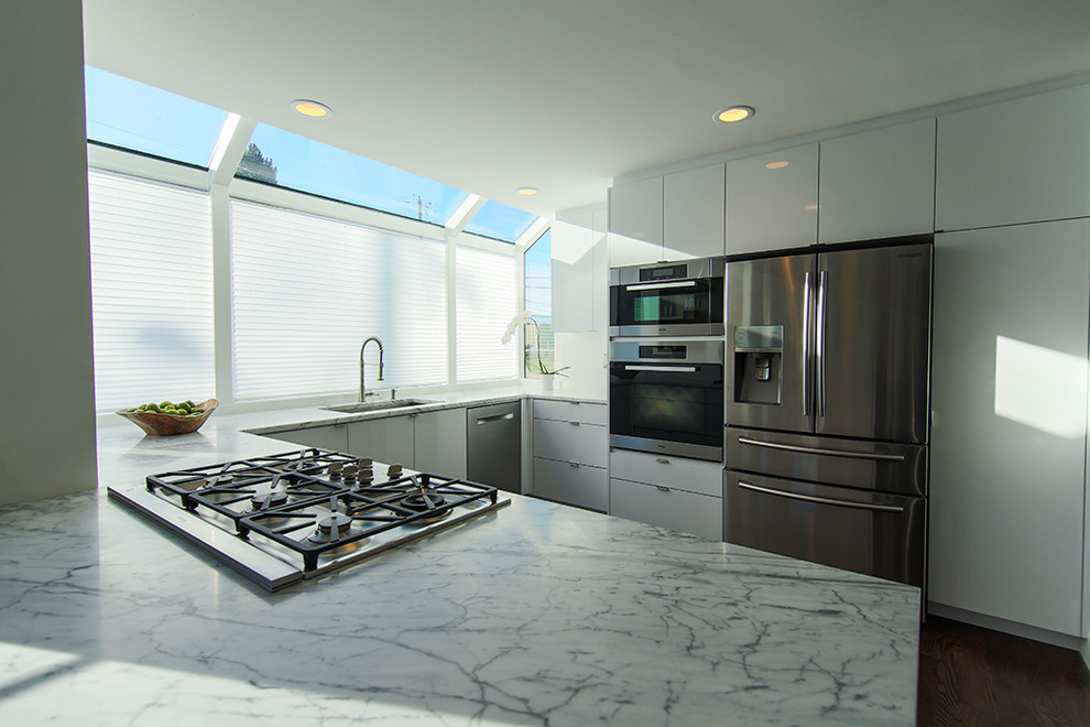 Idéer för att renovera ett funkis u-kök, med en enkel diskho, släta luckor, vita skåp, marmorbänkskiva, rostfria vitvaror och mörkt trägolv