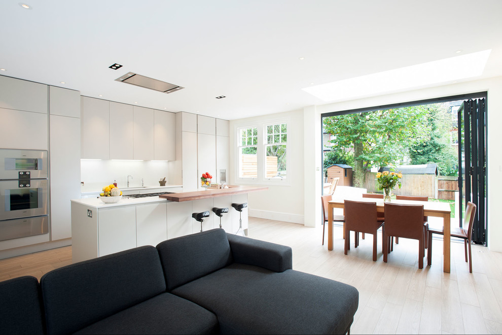 Пример оригинального дизайна: параллельная кухня-гостиная в современном стиле с плоскими фасадами, белыми фасадами, светлым паркетным полом и островом