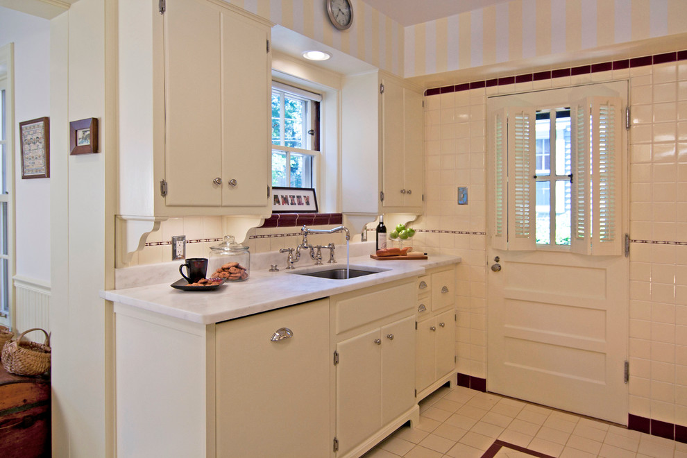 Idée de décoration pour une cuisine parallèle tradition fermée avec un évier encastré, un placard à porte plane, plan de travail en marbre et une crédence blanche.