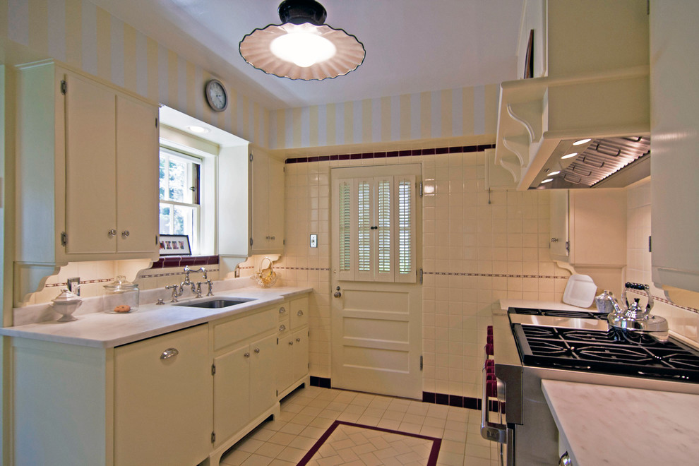 На фото: параллельная, отдельная кухня в классическом стиле с плоскими фасадами, желтыми фасадами, белым фартуком и техникой из нержавеющей стали