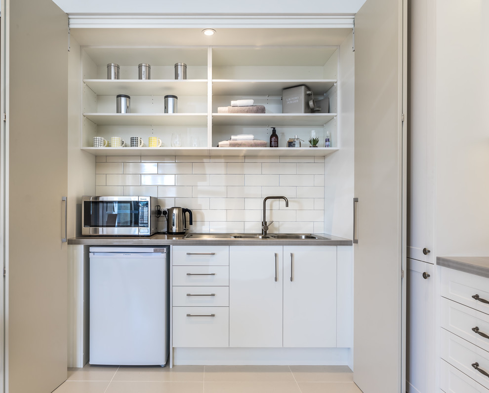 シドニーにある小さなコンテンポラリースタイルのおしゃれなキッチン (ダブルシンク、フラットパネル扉のキャビネット、白いキャビネット、御影石カウンター、白いキッチンパネル、サブウェイタイルのキッチンパネル、白い調理設備、アイランドなし) の写真
