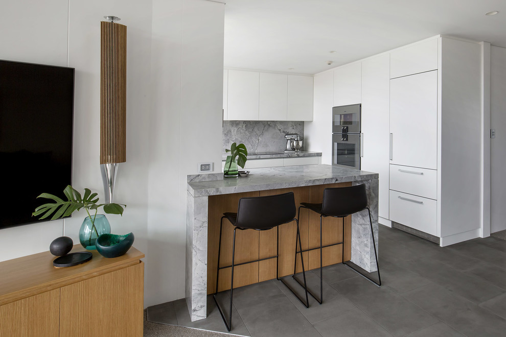 Inredning av ett modernt avskilt, mellanstort grå grått u-kök, med en undermonterad diskho, släta luckor, vita skåp, granitbänkskiva, grått stänkskydd, stänkskydd i sten, rostfria vitvaror, klinkergolv i keramik, en halv köksö och grått golv