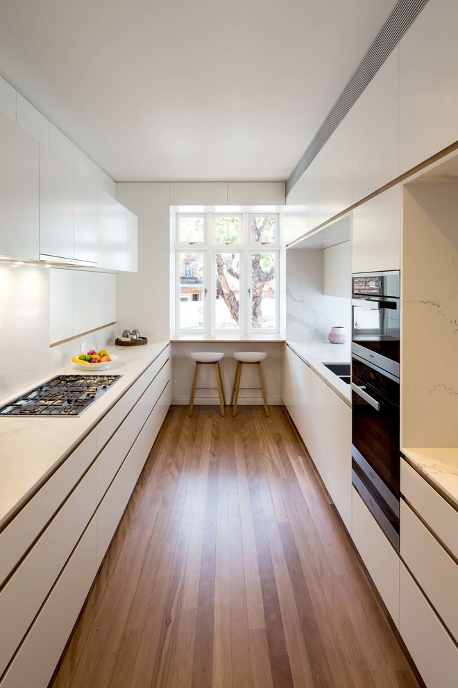 Réalisation d'une cuisine parallèle design avec un évier 2 bacs, un placard à porte plane, des portes de placard blanches, une crédence blanche, un électroménager en acier inoxydable, un sol en bois brun et un sol marron.