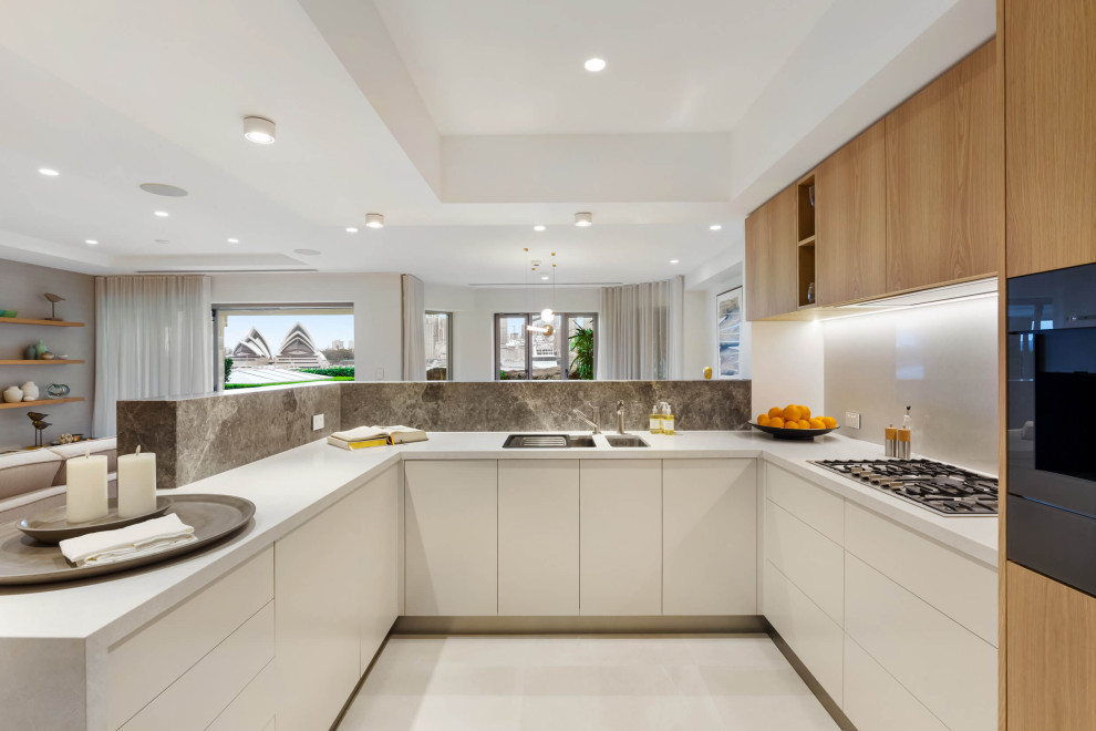 Inspiration for a medium sized contemporary u-shaped open plan kitchen in Sydney with a submerged sink, flat-panel cabinets, limestone worktops, white splashback, engineered quartz splashback, black appliances, ceramic flooring, white floors, a drop ceiling, white cabinets, a breakfast bar and white worktops.