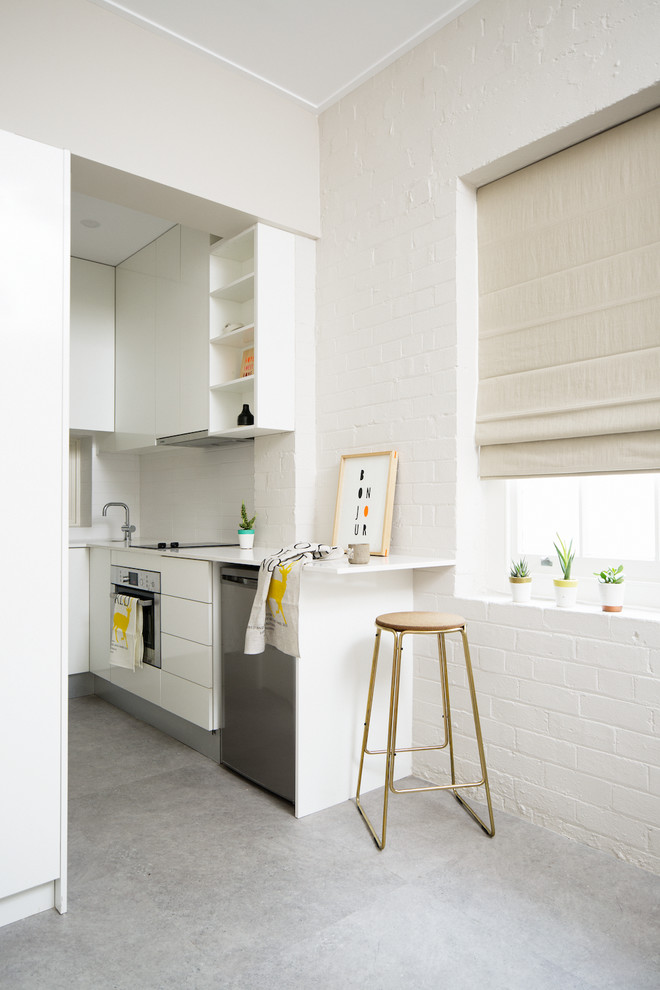 Cette image montre une petite cuisine design avec des portes de placard blanches, un électroménager en acier inoxydable, un placard à porte plane, une crédence blanche, une crédence en feuille de verre et sol en béton ciré.
