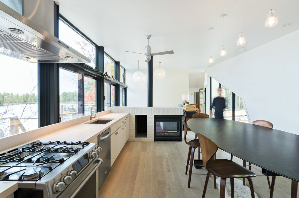 Modern inredning av ett kök och matrum, med en undermonterad diskho, släta luckor, skåp i ljust trä, fönster som stänkskydd, rostfria vitvaror, ljust trägolv och bänkskiva i täljsten