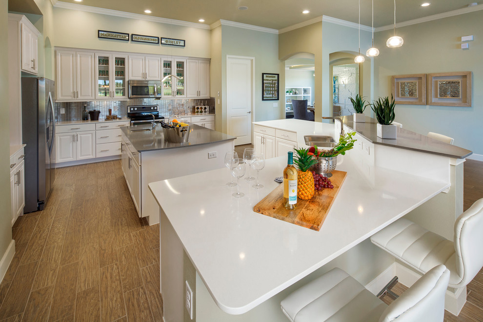 Photo of a large modern l-shaped open plan kitchen in Orlando with a built-in sink, glass-front cabinets, white cabinets, quartz worktops, metallic splashback, glass tiled splashback, stainless steel appliances, plywood flooring and multiple islands.