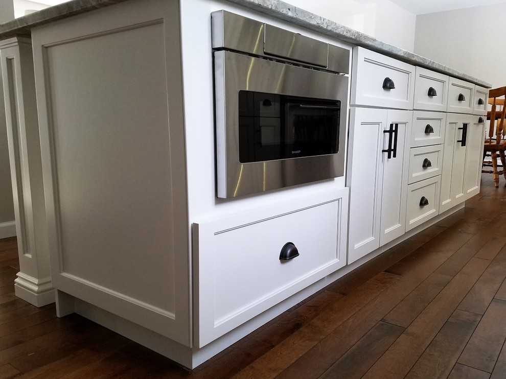 This is an example of a large traditional galley open plan kitchen in Bridgeport with a submerged sink, raised-panel cabinets, white cabinets, granite worktops, brown splashback, ceramic splashback, stainless steel appliances, medium hardwood flooring, an island and brown floors.