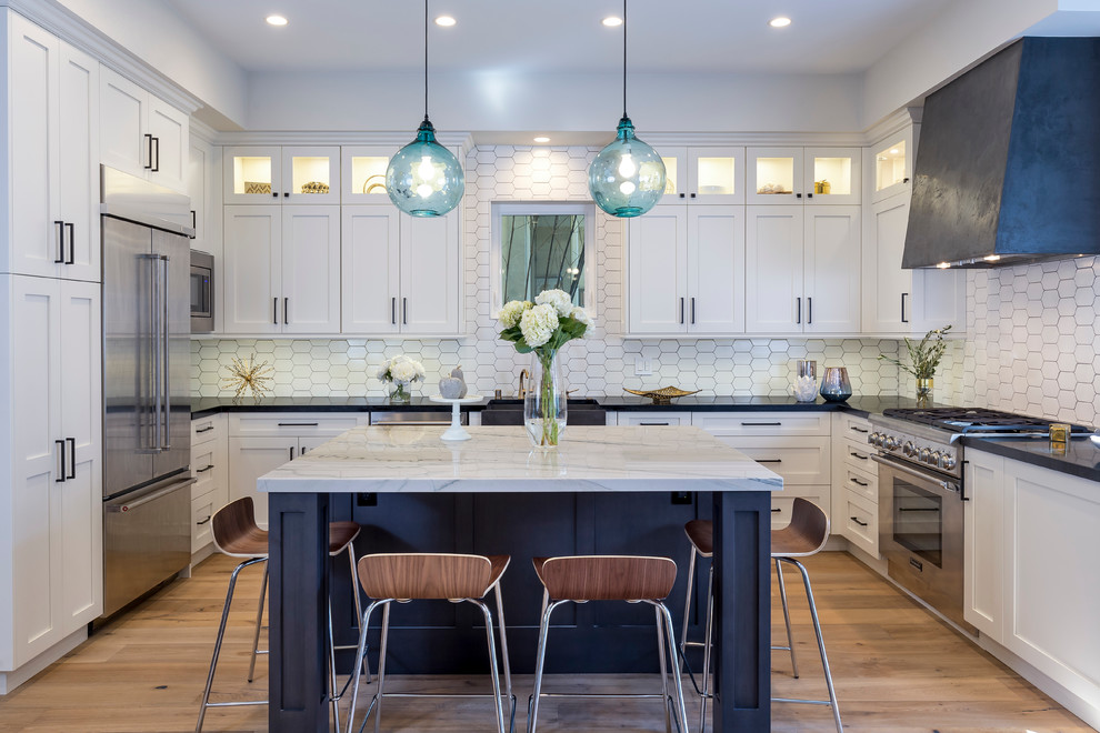 Inspiration for a large traditional u-shaped kitchen/diner in Los Angeles with a belfast sink, shaker cabinets, white cabinets, white splashback, stainless steel appliances, light hardwood flooring and an island.