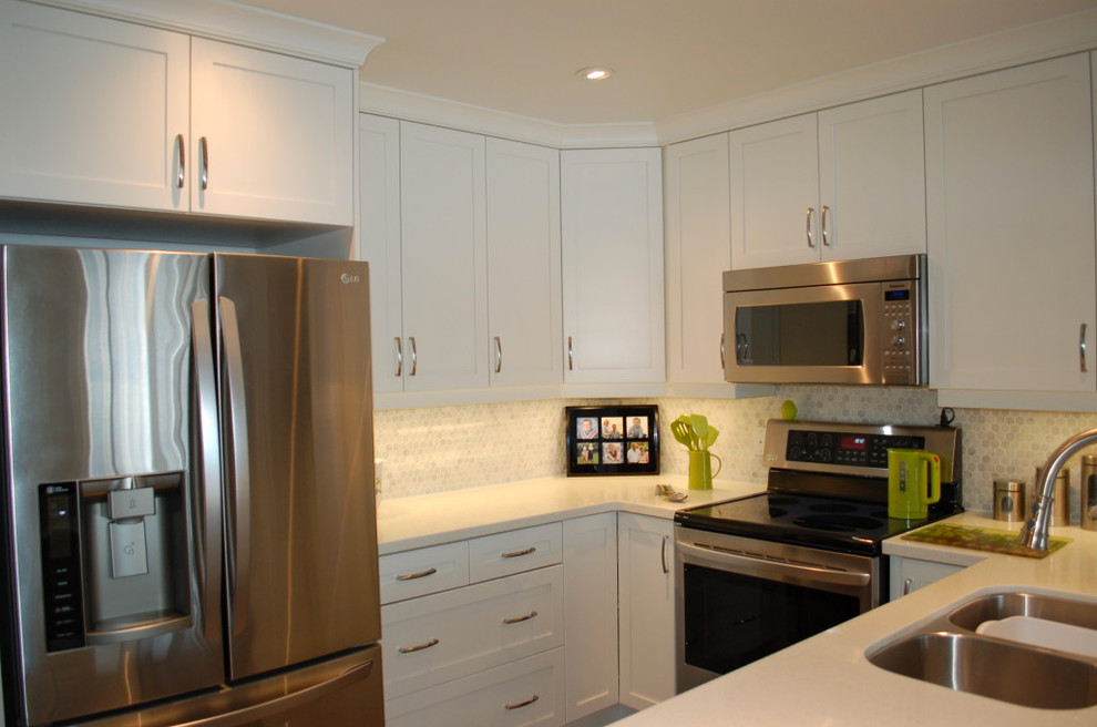 Cette photo montre une petite cuisine ouverte en U avec un évier 2 bacs, des portes de placard blanches, une crédence multicolore, un électroménager en acier inoxydable et une péninsule.