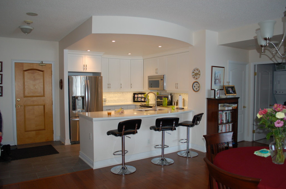 Exempel på ett litet kök, med en undermonterad diskho, vita skåp, vitt stänkskydd, rostfria vitvaror, mellanmörkt trägolv och en halv köksö