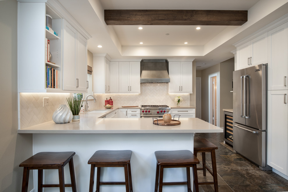 This is an example of a traditional u-shaped kitchen in Los Angeles with a submerged sink, shaker cabinets, white cabinets, beige splashback, stainless steel appliances, a breakfast bar, brown floors and beige worktops.
