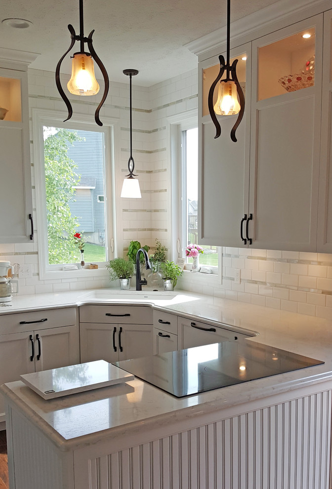 Foto på ett mellanstort lantligt kök, med en undermonterad diskho, släta luckor, vita skåp, bänkskiva i kvarts, vitt stänkskydd, stänkskydd i glaskakel, rostfria vitvaror, laminatgolv och brunt golv