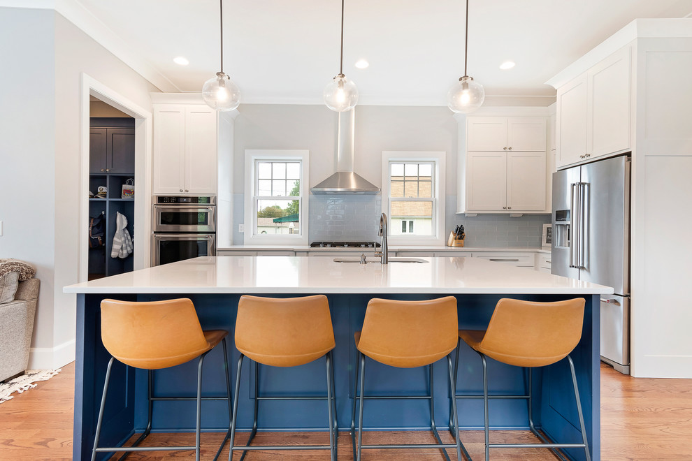 Inspiration for a mid-sized transitional l-shaped light wood floor and beige floor open concept kitchen remodel in Columbus with an undermount sink, shaker cabinets, white cabinets, quartz countertops, blue backsplash, stainless steel appliances, an island, white countertops and subway tile backsplash