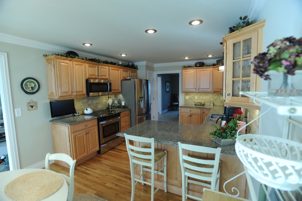 Example of a mid-sized classic u-shaped light wood floor eat-in kitchen design in Other with an undermount sink, raised-panel cabinets, light wood cabinets, granite countertops, beige backsplash, stone tile backsplash, stainless steel appliances and a peninsula