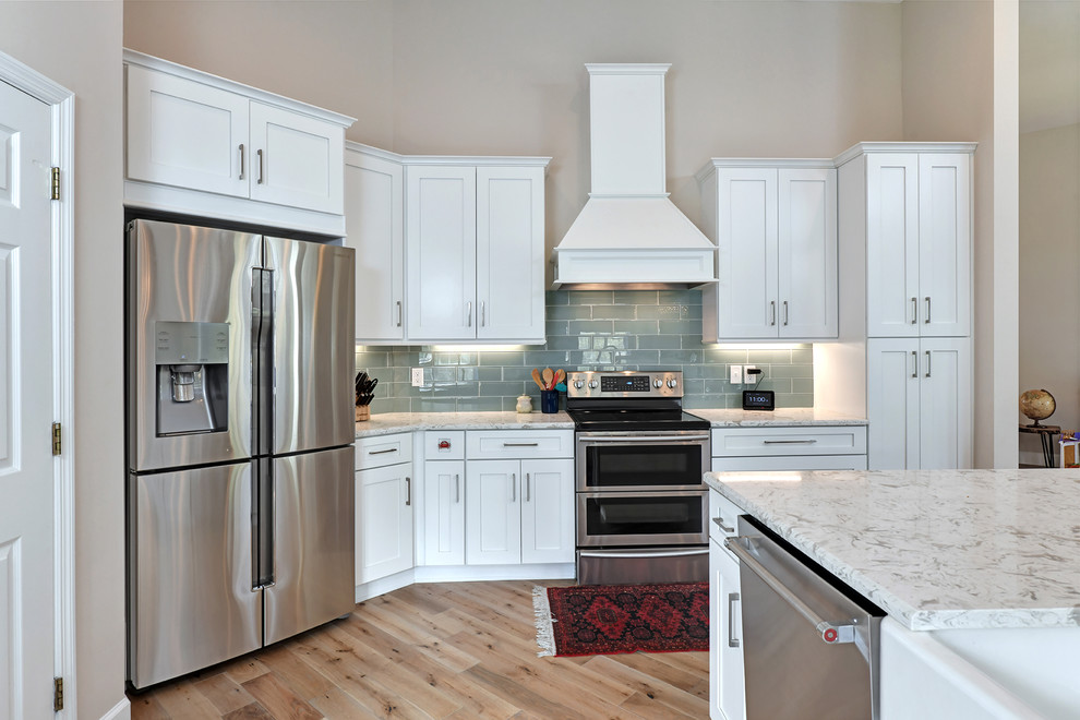 Foto på ett mellanstort funkis vit linjärt kök med öppen planlösning, med en undermonterad diskho, skåp i shakerstil, vita skåp, bänkskiva i kvarts, blått stänkskydd, stänkskydd i glaskakel, rostfria vitvaror, ljust trägolv och en köksö
