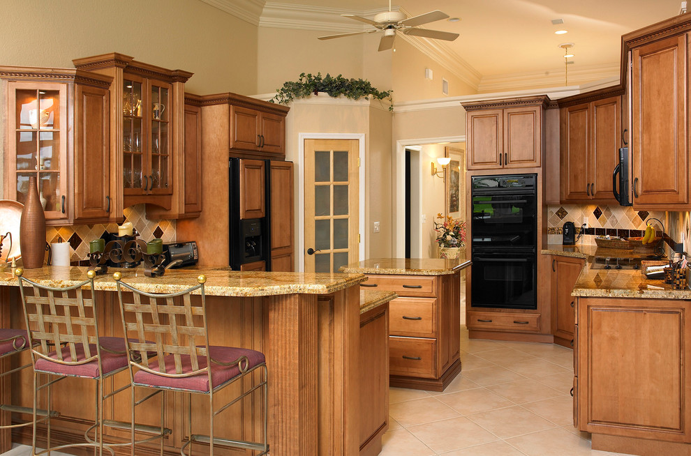 Photo of a medium sized traditional u-shaped kitchen in Miami with granite worktops, a submerged sink, raised-panel cabinets, medium wood cabinets, multi-coloured splashback, porcelain splashback, black appliances, ceramic flooring, an island, beige floors and brown worktops.