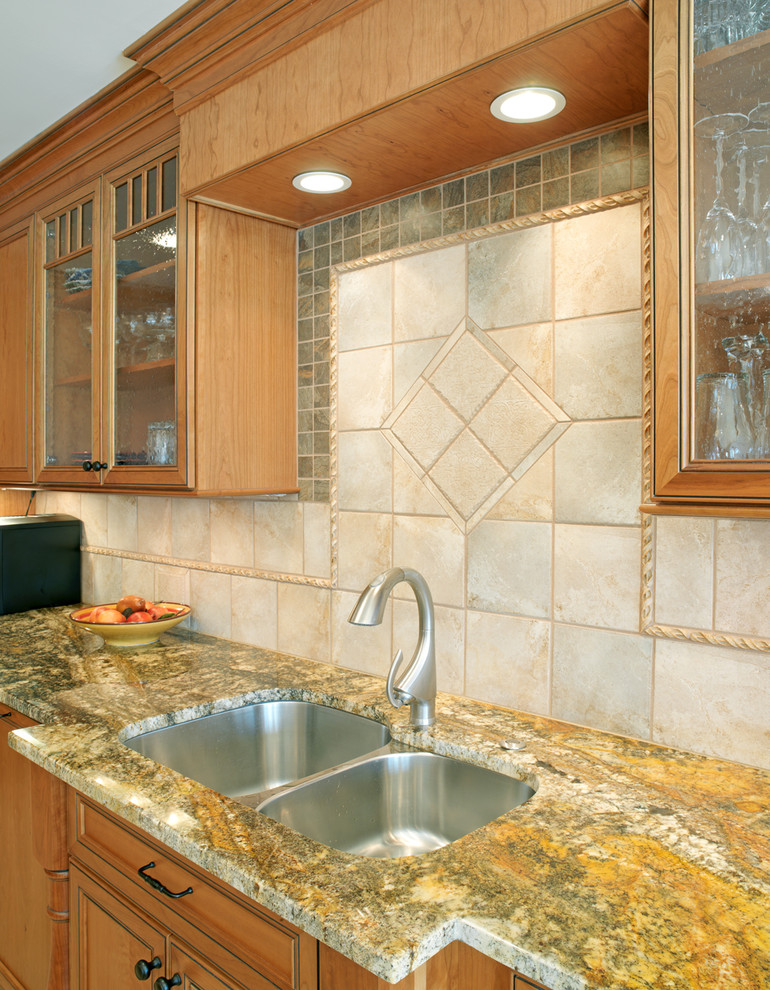 Foto på ett kök, med en undermonterad diskho, luckor med infälld panel, skåp i mellenmörkt trä, granitbänkskiva, beige stänkskydd, stänkskydd i keramik, rostfria vitvaror, klinkergolv i keramik och en köksö