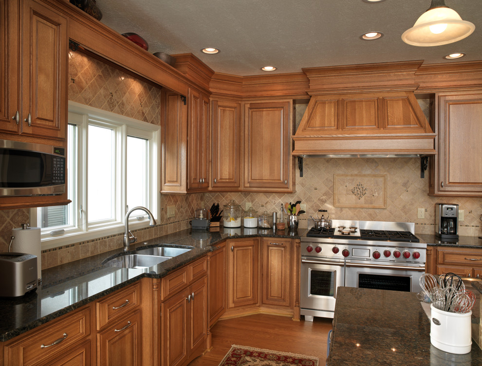 Example of a classic medium tone wood floor eat-in kitchen design in Columbus with an undermount sink, raised-panel cabinets, medium tone wood cabinets, granite countertops, beige backsplash, ceramic backsplash, stainless steel appliances and an island