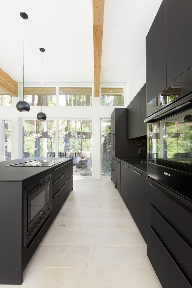 Réalisation d'une cuisine parallèle minimaliste avec un évier encastré, un placard à porte plane, des portes de placard noires, un électroménager noir, îlot, un sol beige et plan de travail noir.