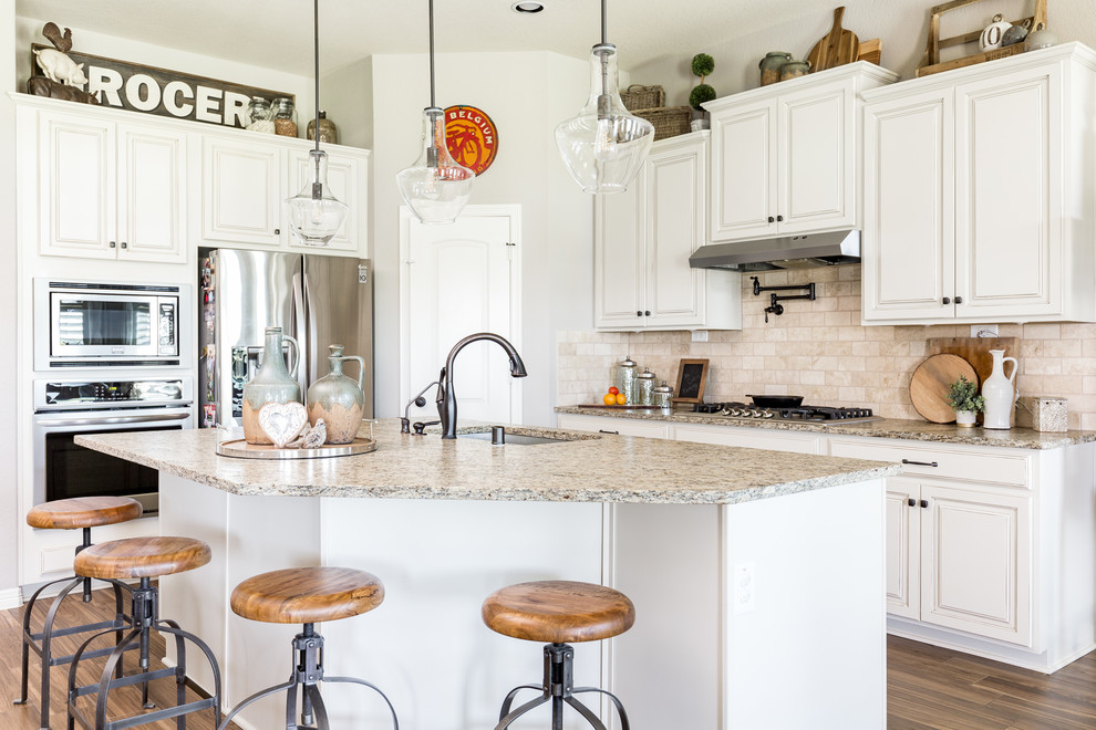 Inspiration for a timeless l-shaped dark wood floor and brown floor kitchen remodel in Houston with an undermount sink, raised-panel cabinets, white cabinets, beige backsplash, stainless steel appliances, an island and beige countertops