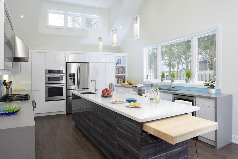 Bild på ett funkis u-kök, med en dubbel diskho, släta luckor, vita skåp, bänkskiva i kvarts, blått stänkskydd, glaspanel som stänkskydd, rostfria vitvaror, mörkt trägolv och en köksö