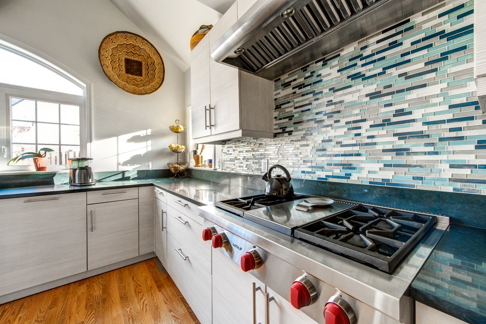 Immagine di una cucina moderna con ante lisce, ante bianche, top in quarzo composito, paraspruzzi blu, paraspruzzi con piastrelle di vetro, elettrodomestici in acciaio inossidabile e pavimento in legno massello medio