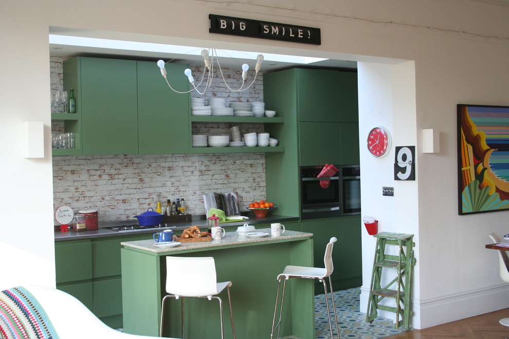 This is an example of a medium sized classic single-wall open plan kitchen in London with an integrated sink, flat-panel cabinets, green cabinets, stainless steel worktops, multi-coloured splashback, glass sheet splashback, stainless steel appliances, light hardwood flooring and an island.