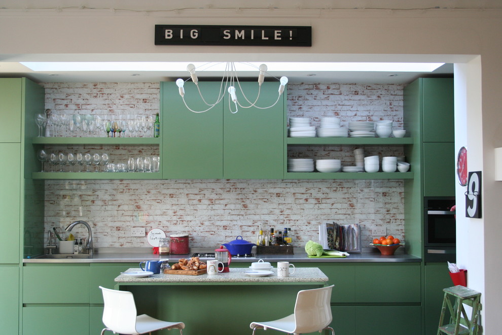 This is an example of a medium sized classic kitchen/diner in London with flat-panel cabinets, green cabinets, an integrated sink, stainless steel worktops, multi-coloured splashback, stainless steel appliances and an island.