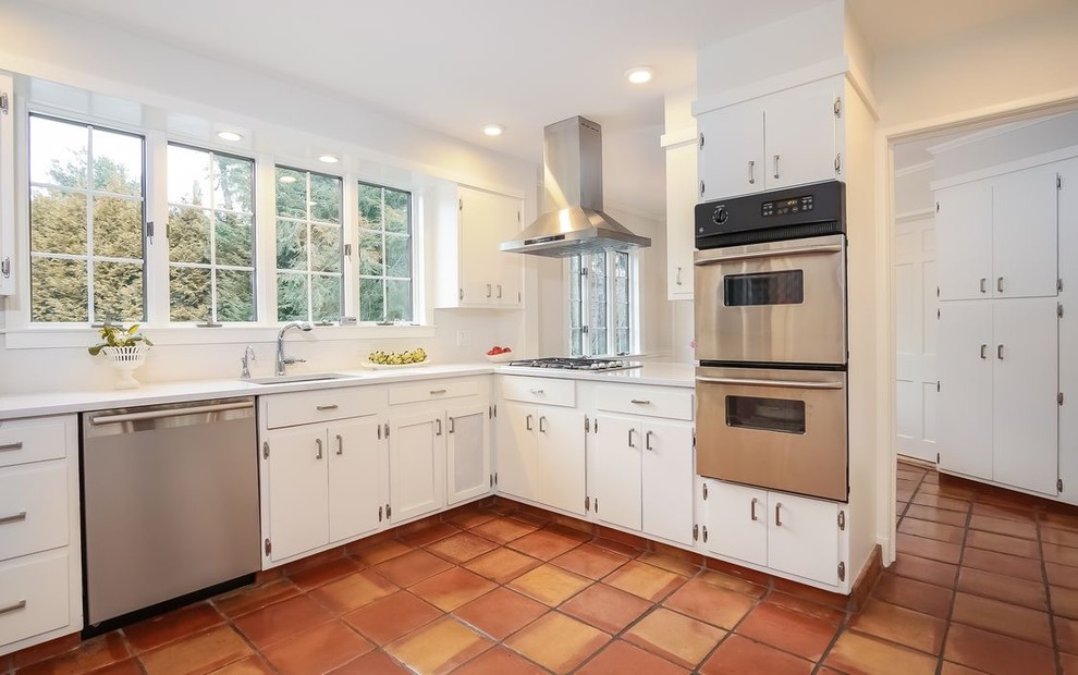 Elegant terra-cotta tile and multicolored floor kitchen photo in New York with an undermount sink, flat-panel cabinets, white cabinets, solid surface countertops, white backsplash, stainless steel appliances, no island and white countertops