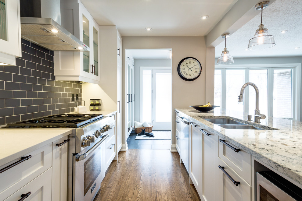 Photo of a medium sized classic galley open plan kitchen in Other with a submerged sink, shaker cabinets, white cabinets, grey splashback, stainless steel appliances, medium hardwood flooring, marble worktops, metro tiled splashback and a breakfast bar.