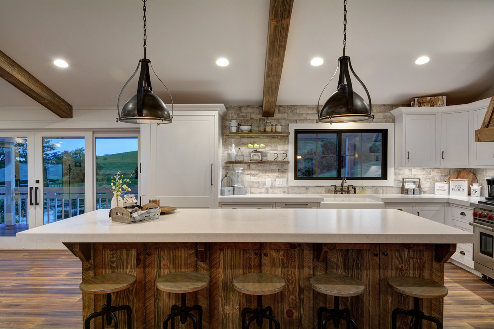 Immagine di una cucina country con lavello stile country, ante in stile shaker, ante bianche, paraspruzzi beige, elettrodomestici da incasso, parquet scuro, pavimento marrone e top bianco