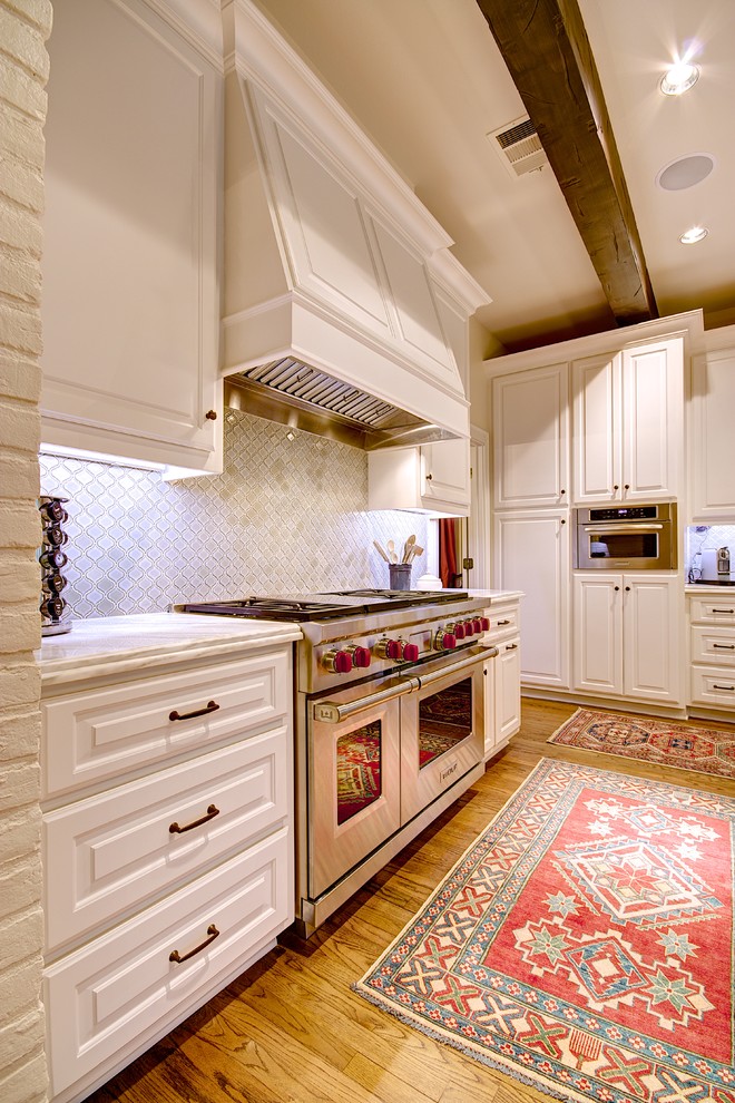 Eat-in kitchen - large traditional l-shaped light wood floor eat-in kitchen idea in Austin with raised-panel cabinets, white cabinets, marble countertops, white backsplash, glass tile backsplash, stainless steel appliances and an island