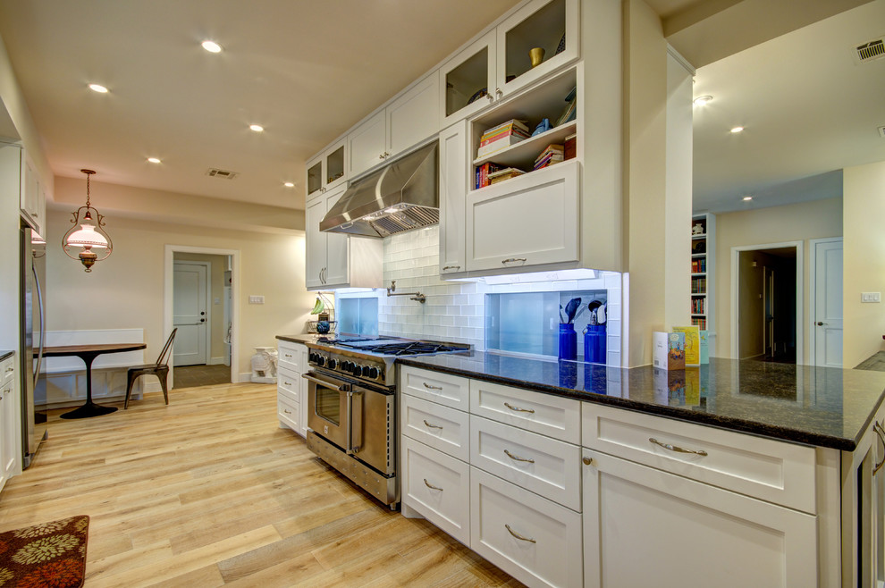 Mid-sized transitional galley light wood floor eat-in kitchen photo in Austin with an undermount sink, shaker cabinets, white cabinets, granite countertops, white backsplash, glass tile backsplash, stainless steel appliances and no island