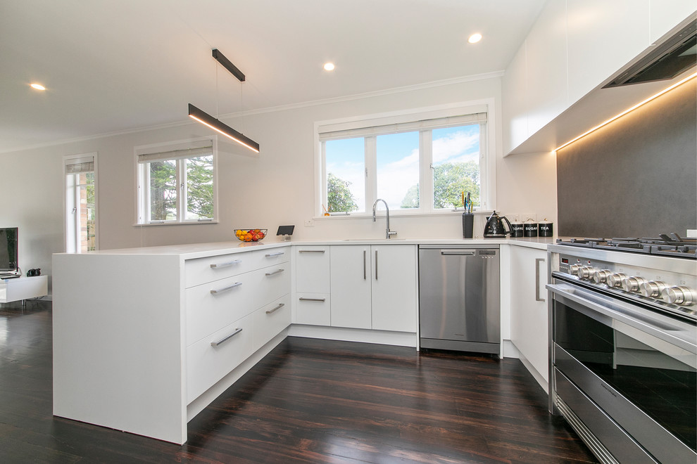 Inspiration for a mid-sized contemporary u-shaped dark wood floor and brown floor eat-in kitchen remodel in Auckland with a drop-in sink, white cabinets, quartz countertops, gray backsplash, porcelain backsplash, stainless steel appliances, a peninsula and white countertops