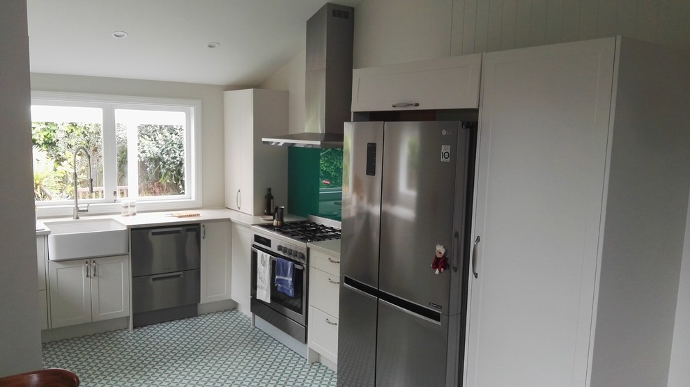 Medium sized classic u-shaped kitchen in Auckland with a built-in sink, shaker cabinets, white cabinets, engineered stone countertops, green splashback, glass sheet splashback, stainless steel appliances, lino flooring, white floors and white worktops.