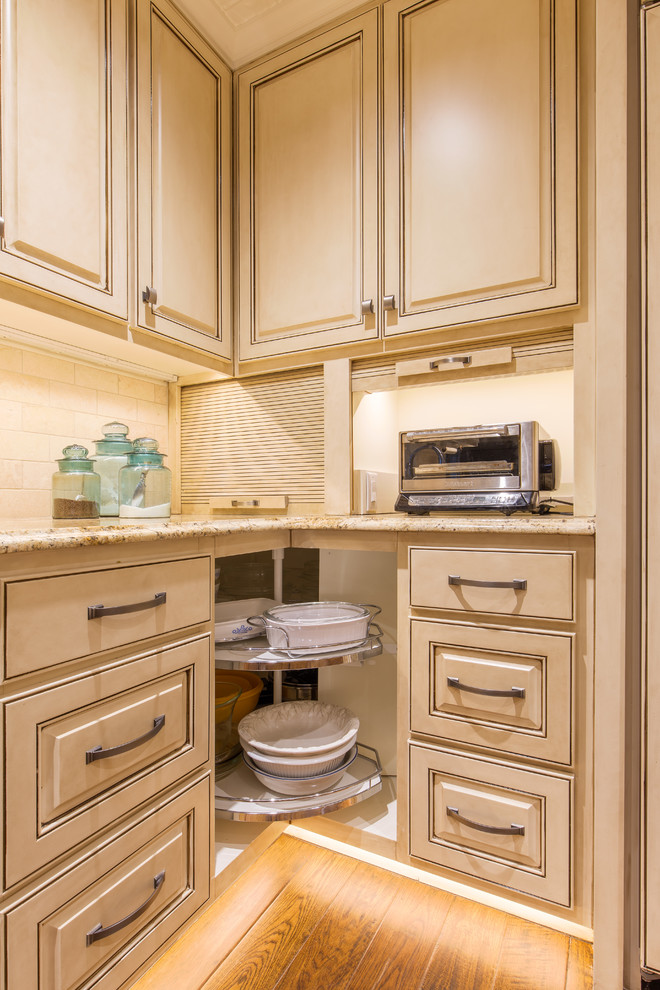 Exempel på ett avskilt, stort klassiskt u-kök, med en dubbel diskho, luckor med upphöjd panel, vita skåp, granitbänkskiva, beige stänkskydd, stänkskydd i stenkakel, integrerade vitvaror, mellanmörkt trägolv och en köksö