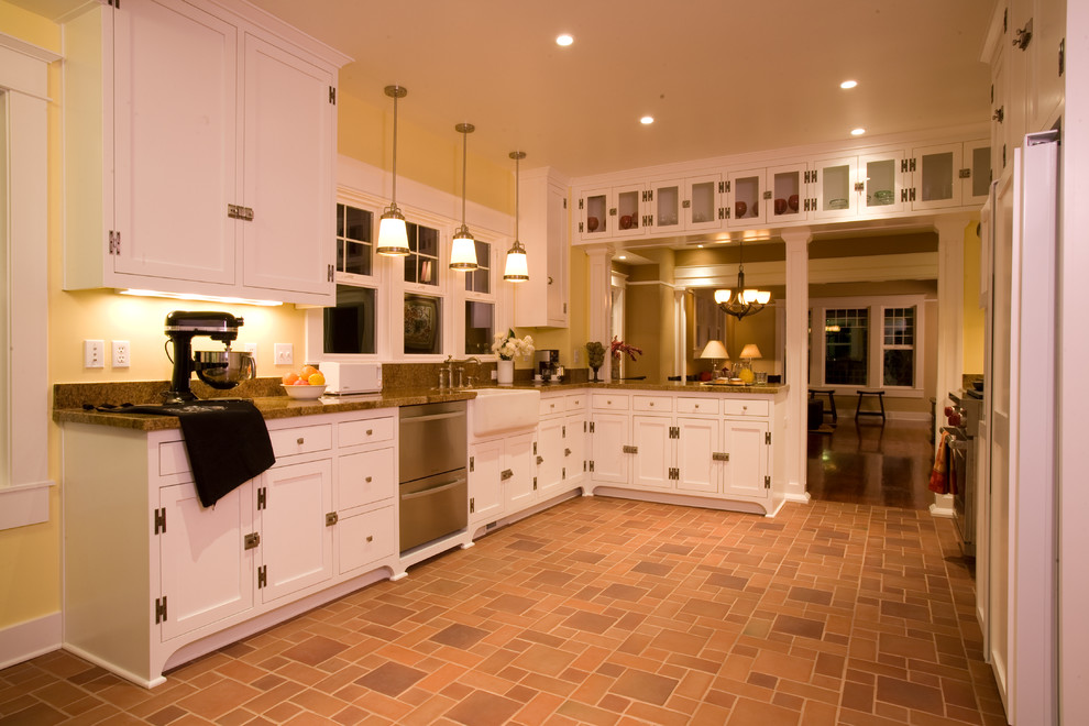 Amerikansk inredning av ett mellanstort kök, med en rustik diskho, luckor med infälld panel, vita skåp, granitbänkskiva, stänkskydd i sten, rostfria vitvaror och tegelgolv