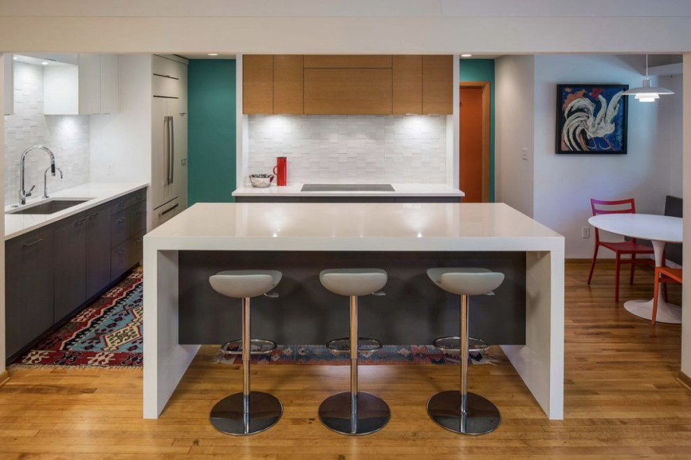 Small contemporary galley kitchen/diner in Minneapolis with flat-panel cabinets, white cabinets, composite countertops, white splashback, ceramic splashback, white appliances, light hardwood flooring, an island, yellow floors and white worktops.