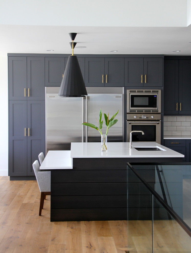 Große Klassische Küche mit Küchenrückwand in Weiß, Küchengeräten aus Edelstahl, braunem Holzboden, Kücheninsel, Unterbauwaschbecken, Schrankfronten im Shaker-Stil und Rückwand aus Metrofliesen in Vancouver