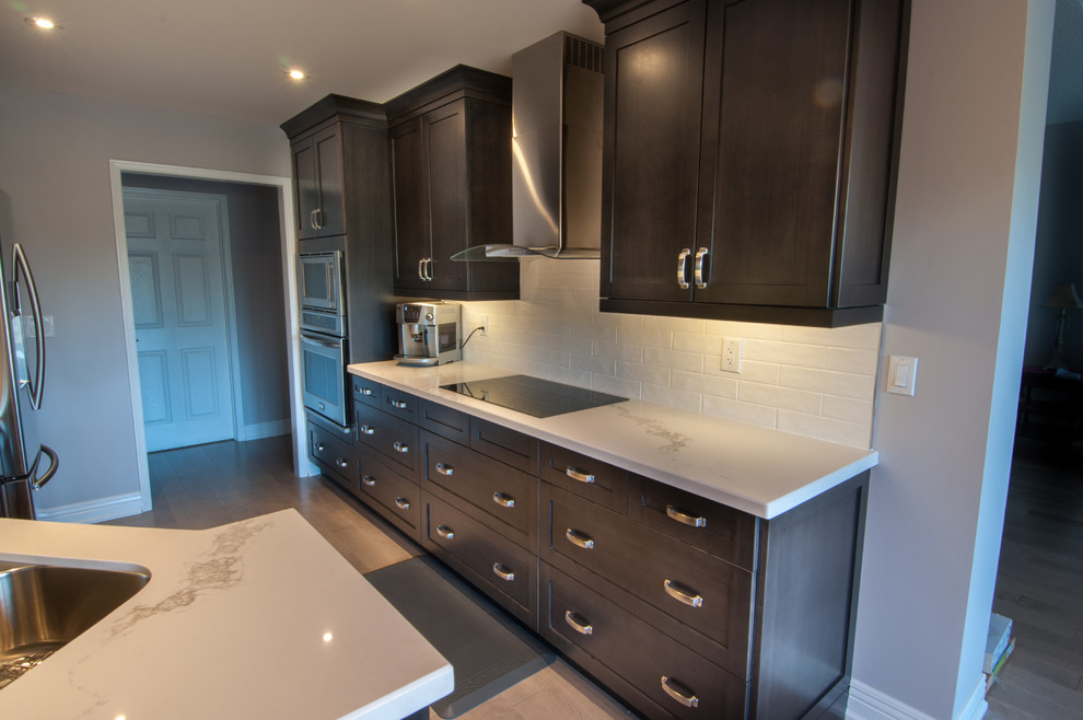 Example of a small minimalist galley dark wood floor enclosed kitchen design in Toronto with a double-bowl sink, shaker cabinets, dark wood cabinets, white backsplash, subway tile backsplash, stainless steel appliances, no island and marble countertops