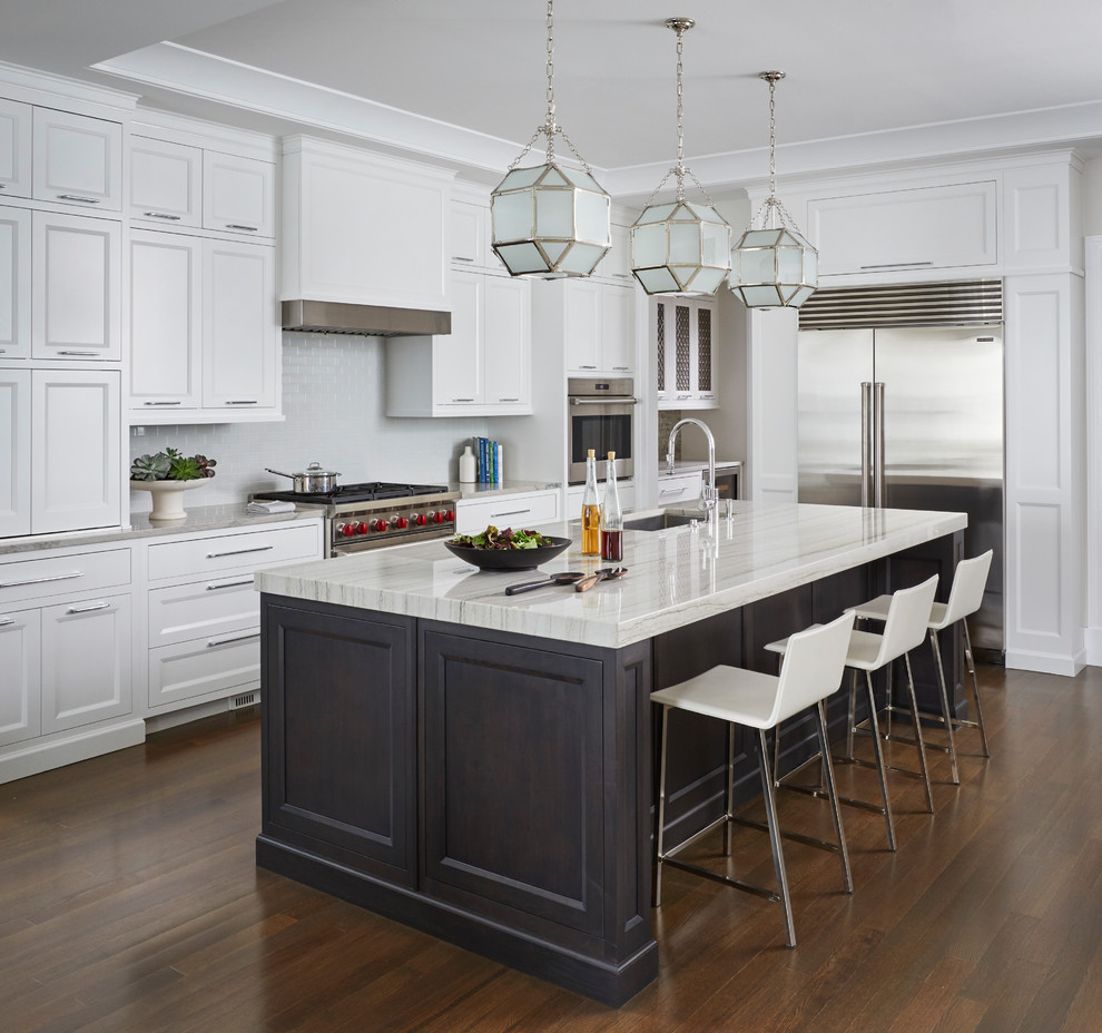 Klassisk inredning av ett mellanstort flerfärgad flerfärgat kök, med vita skåp, marmorbänkskiva, vitt stänkskydd, rostfria vitvaror, mörkt trägolv, en köksö, brunt golv, en undermonterad diskho och skåp i shakerstil