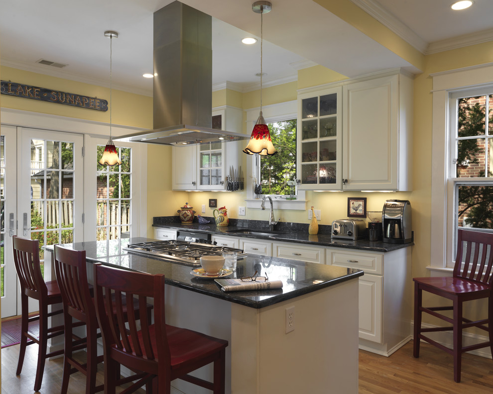 На фото: кухня в классическом стиле с фасадами с выступающей филенкой, белыми фасадами, черным фартуком и барной стойкой