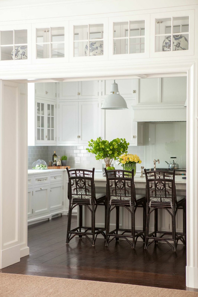 Exempel på ett klassiskt kök, med luckor med infälld panel, vita skåp, vitt stänkskydd, mörkt trägolv och en köksö
