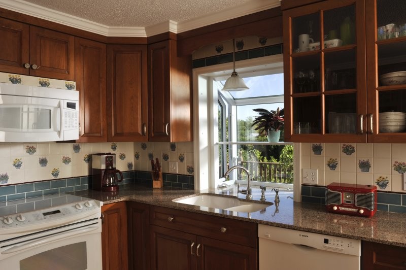 Elegant l-shaped kitchen pantry photo in New York with a double-bowl sink, glass-front cabinets, medium tone wood cabinets, granite countertops, multicolored backsplash, porcelain backsplash and white appliances