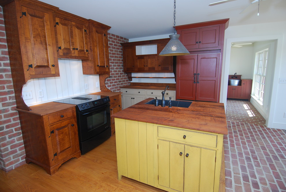 Lantlig inredning av ett kök, med en rustik diskho, skåp i shakerstil, gula skåp, träbänkskiva, vitt stänkskydd, integrerade vitvaror, tegelgolv och en köksö