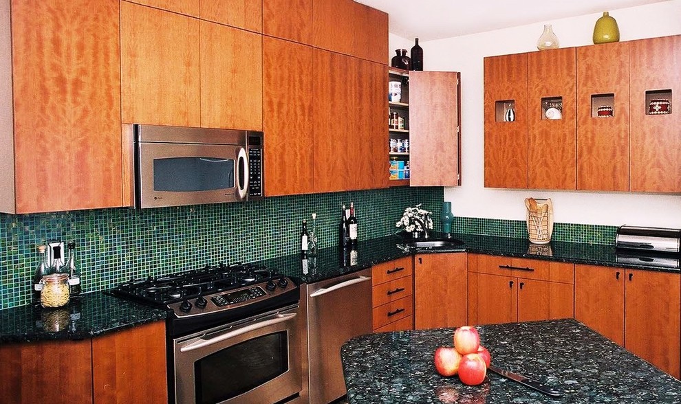 Bild på ett avskilt, mellanstort funkis l-kök, med en undermonterad diskho, släta luckor, skåp i mellenmörkt trä, granitbänkskiva, grönt stänkskydd, stänkskydd i glaskakel, rostfria vitvaror, klinkergolv i keramik och en halv köksö